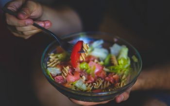 A vibrant bowl of healthy pasta salad with fresh vegetables in a casual setting.